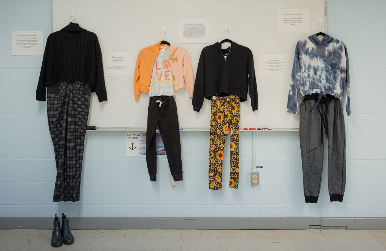 A classroom has multiple outfits hanging on the wall during an exhibit.