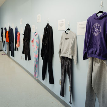 A classroom has multiple outfits hanging on the wall during an exhibit.