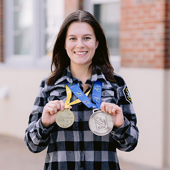 Olivia stands while holding a gold medal in her left hand and a Best in Region medal in her right hand.