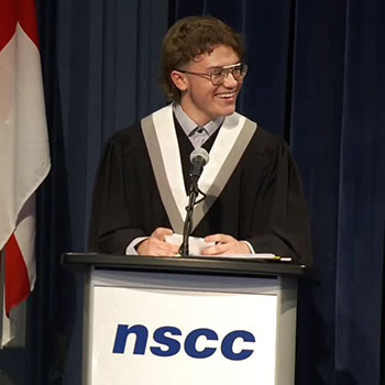 Quinn Legg, wearing a graduation cap and gown, smiles during valedictorian speech