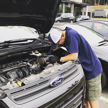 Quinn Legg standing in front of a vehicle working under the engine hood