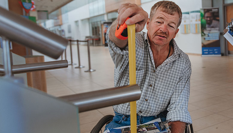 Man in wheelchair taking a measurement of something.