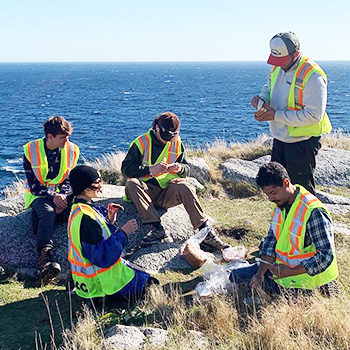 NRET students sitting on rocks and eating lunch by the ocean
