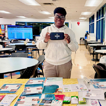 Image show sa student behind a display they set up that promotes student wellness.