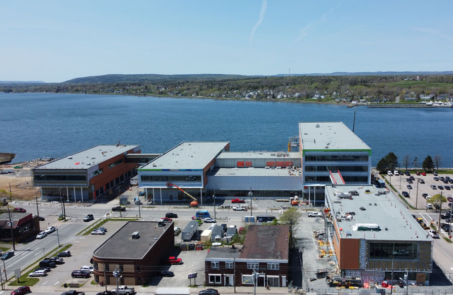 A drone view shows a new campus building under construction, between the ocean and downtown area of Cape Breton.
