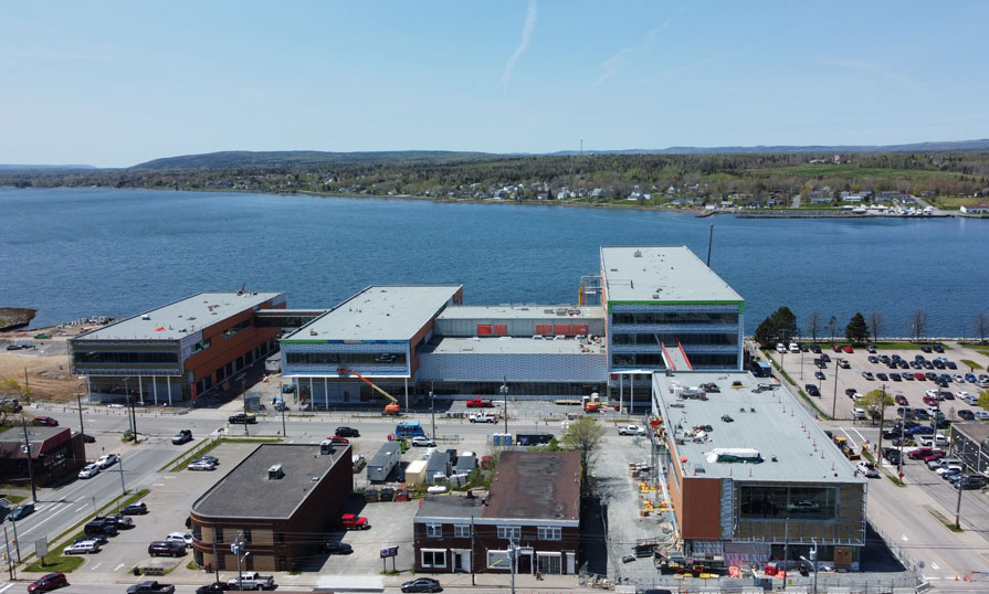 A drone view shows a new campus building under construction, between the ocean and downtown area of Cape Breton.