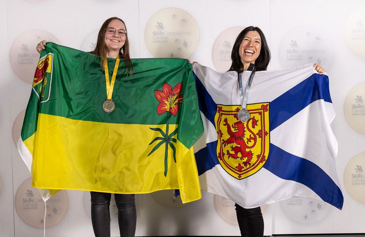 A person is smiling and holding up a Nova Scotia flag. 