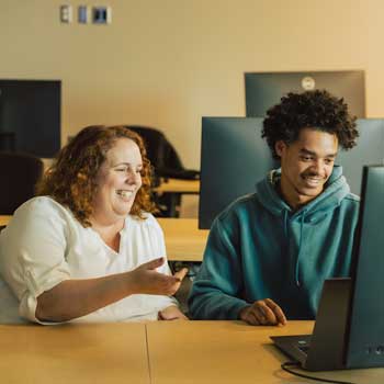 Anna-Marie Roper, TAP Coordinator sitting next to student, Tavarion Burke while facing a computer and smiling