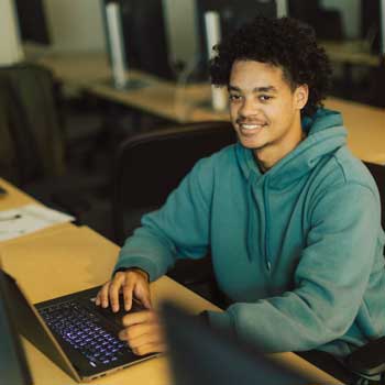 Student wearing gray hoodie sitting in front of computer 