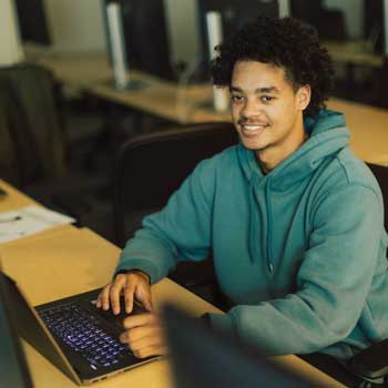 Student wearing gray hoodie sitting in front of computer