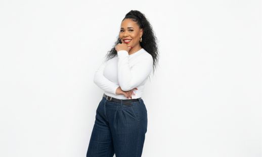 Image shows a photo of a woman wearing jeans and a white long sleeve, smiling at the camera.