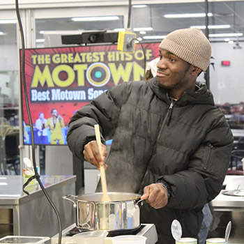 Victor stirs a large stock pot in an industrial kitchen.