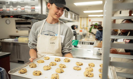 Youth placing a baking sheet full of cookies in an oven