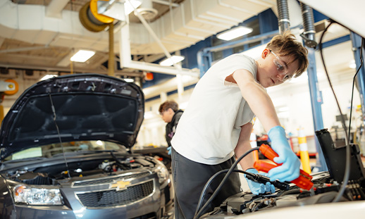 Youth standing under the hood of a car while holding charging cables