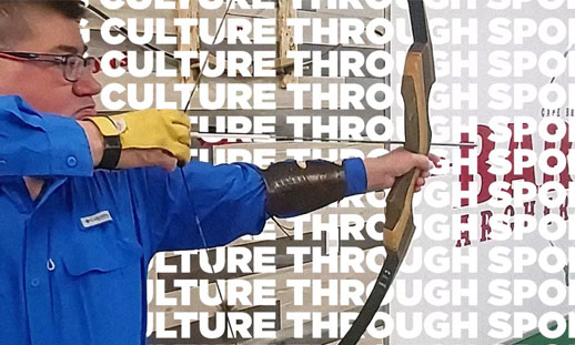 A man with a bow and arrow aims to the right. In the background it reads "sharing culture through sport."