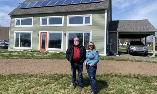 Photo of two people standing outside a home with solar panels on the roof.