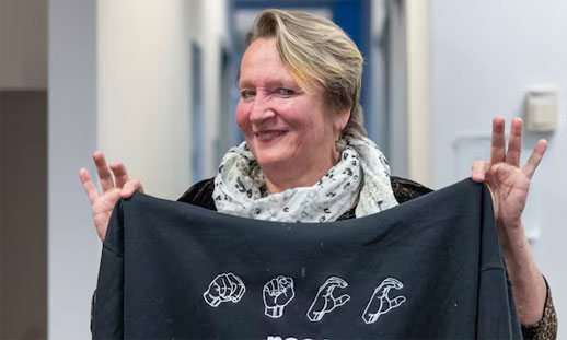 A person is holding up a t-shirt that has 'NSCC' spelled out with sign language.