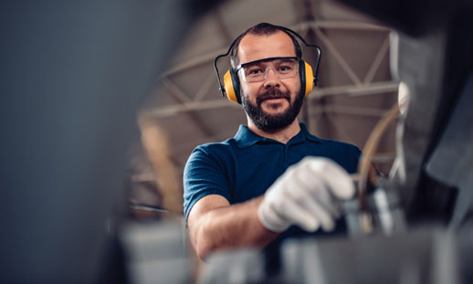 A man works at a machine and wears ear protection.