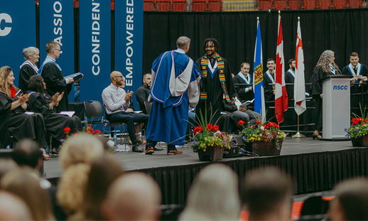 A student receives their diploma from the College's president while walking across the stage.