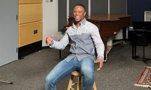 A person is sitting on a stool in a recording studio.