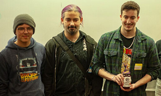 Three students stand together for a photo, holding an award.