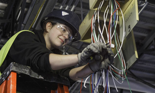 A person is working on wires and wearing safety gear.