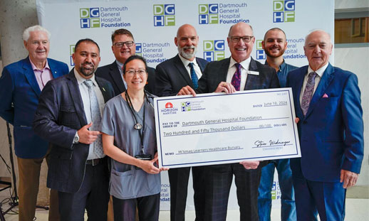 A group of people stand together holding a large cheque.