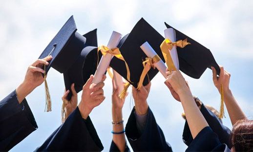 A group of graduates hold their grad caps together towards the sky.