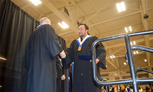 A graduate is about to step off stage with his diploma as he shakes the hands of his faculty members. 
