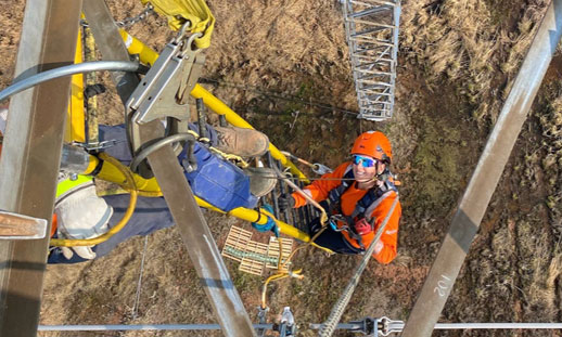 Image shows someone climbing a powerline in uniform.