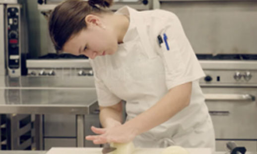 A chef is working in a kitchen, cutting up ingredients.