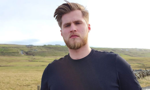 Image shows a person standing outside near a field.