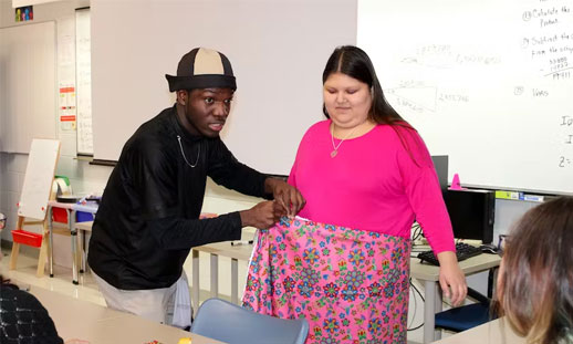Image shows a person fitting another person with fabric to make a skirt.