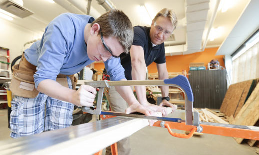 A youth is using a saw to cut a piece of wood in a workshop.