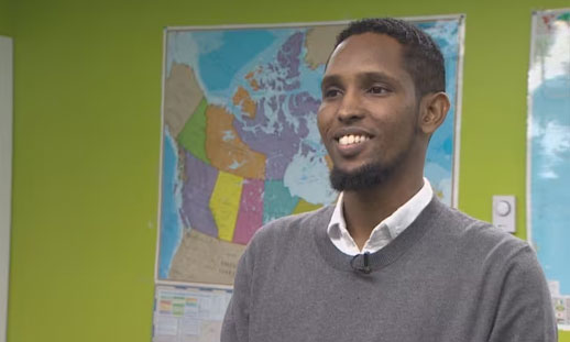 Mohamed Hussein is pictured. He is standing in front of a large map.
