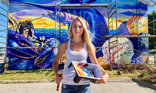 Danielle Mahood is pictured in front of a mural she has painted on a building.