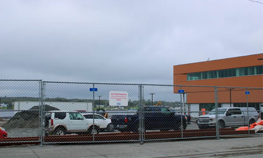 A parking lot behind a metal fence is shown on a gloomy, cloudy day.
