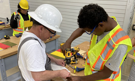 Two students are working in a trades shop wearing construction safety gear.
