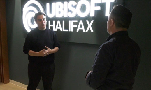 Two men stand in front of a LED logo on a wall that reads, "Ubisoft Halifax."