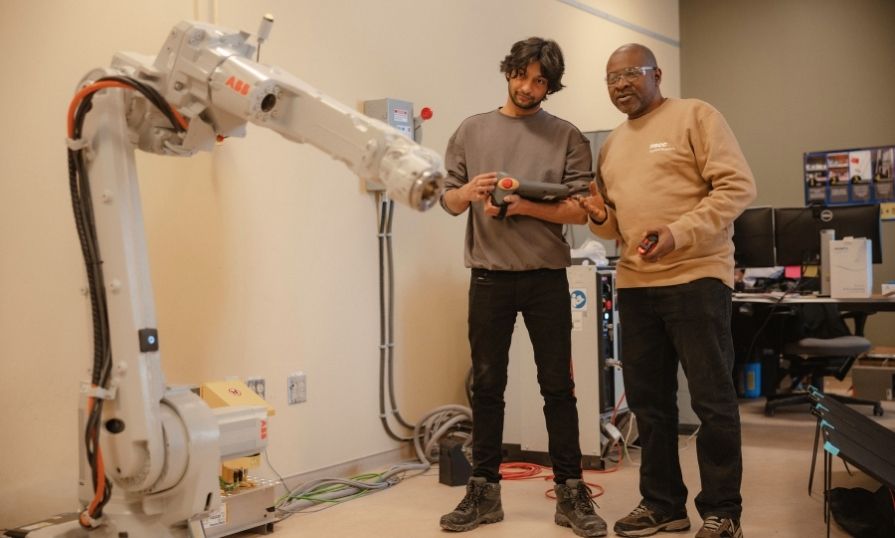 A student research assistant receives hands-on training with an industrial robotic arm in a research lab.