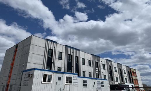 A building under construction is shown, standing in front of a bright blue sky with lots of clouds.
