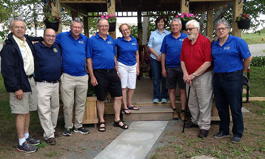 A group of individuals in warm-weather clothing stand in front of a newly constructed gazebo.