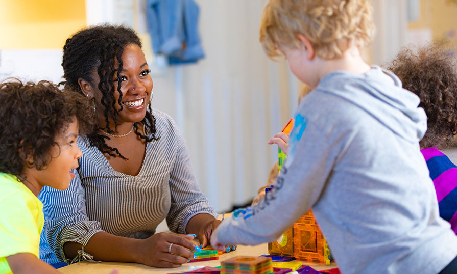 Woman speaks with group of young children around a table. They are smiling.