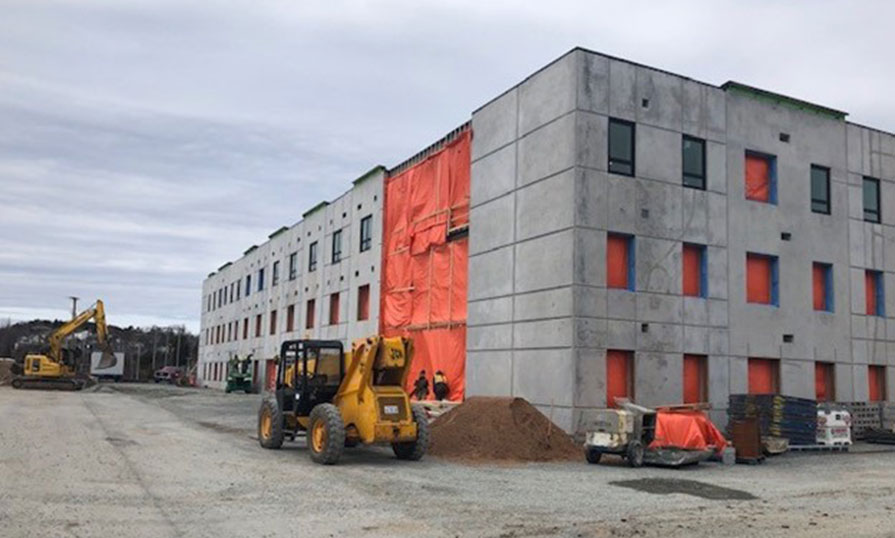 A construction site of a student housing build on a gloomy day shows walls built and window installation in progress.