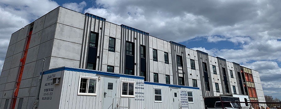 A building under construction is shown, standing in front of a bright blue sky with lots of clouds.