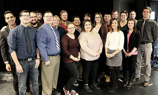 A group of 19 individuals stands close together and smiles for a photo.