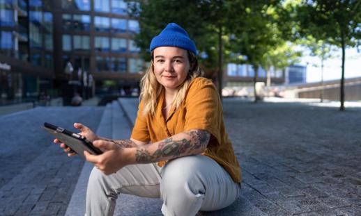 Anisa Francoeur sits outside on a staircase and smiles while holding an ipad.