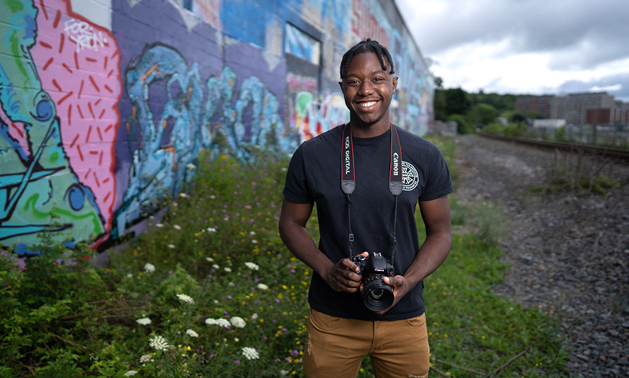 Keandre Johnson is pictured. He is outdoors and has a camera hung around his neck.