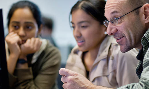 Two women and a man crowd around a computer monitor.