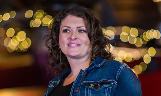 A woman in a jean jacket smiles and looks to the left. The background it blurry.